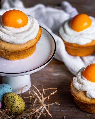 Vier helle Muffins mit Frischkäse-Creme und Aprikosen auf Holzuntergrund