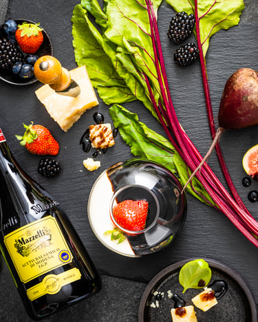 Balsamico-Flaschen, Beeren, Parmesan und mehr liegen auf dunklem Untergrund