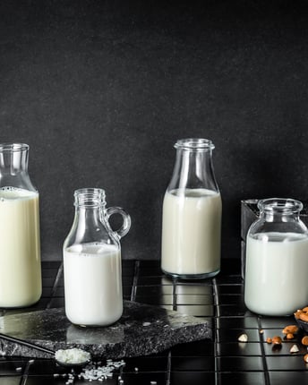 Sechs verschiedene pflanzliche Milch-Alternative in kleinen Glasflaschen stehen vor einem schwarzen Hintergrund