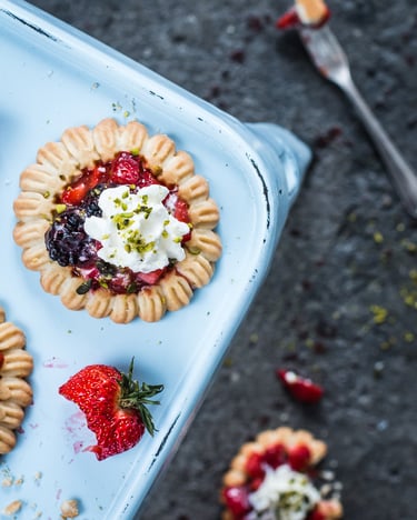 Schnelle Tartelettes mit Beerenfüllung und einer Sahnehaube mit Pistazien auf einem Backblech und eine angebissene Erdbeere