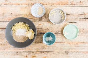 Butter, Semmelbrösel, Mehl und Käse in einer grauen Schale. Daneben kleine Schüsseln mit Resten der Zutaten