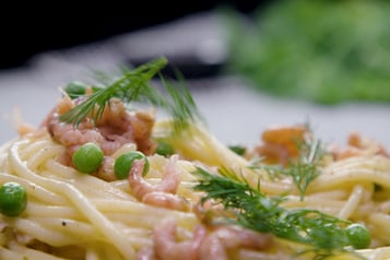 Eine Nahaufnahme von Spaghetti mit Krabben, Erbsen und Dill.