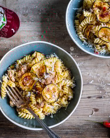 Pasta mit Thunfisch und Zucchini in zwei Porzellanschüsseln auf hellem Holzuntergrund