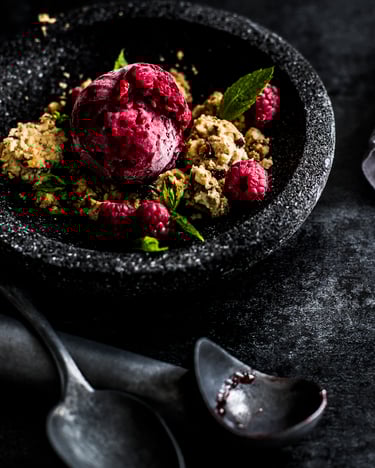 Frozen Joghurt mit Himbeeren und Nusscrumble in einer dunklen Steinschale auf dunklem Untergrund.