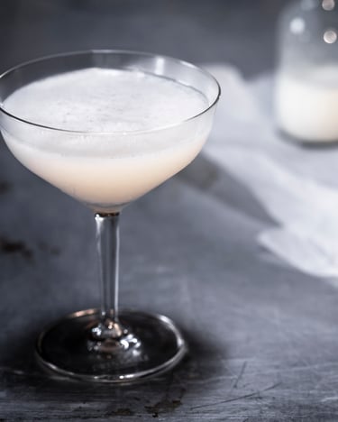 Ein Buttermilk Margarita mit Tequila und Zitrone in einer Cocktailschale auf grauem Untergrund.