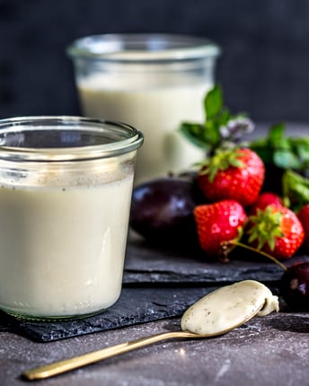 2 Gläser Panna Cotta, daneben liegen Beeren und ein Löffel