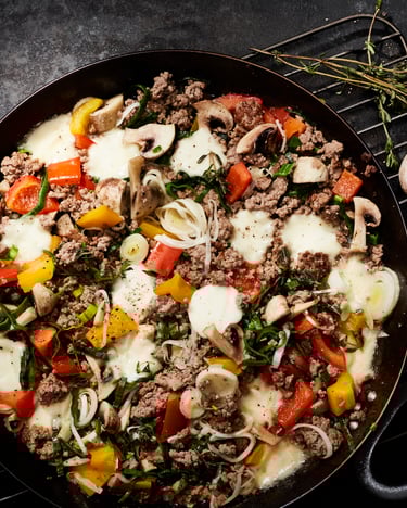 Hackfleischpfanne mit Gemüse und Mozzarella überbacken in einer schwarzen Pfanne steht auf einem Gitter