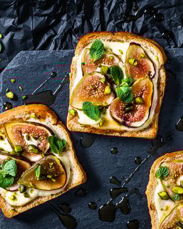 Drei Scheiben Custard Toast mit Feigen und Pistazien vor dunklem Hintergrund