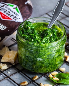 Pesto alla genovese in kleinem Glasgefäß auf Gitter mit Zutaten im Hintergrund