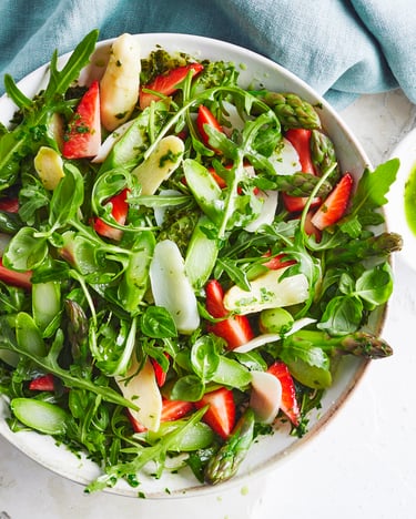 In einer weißen Schale befindet sich Spargelsalat mit Erdbeeren, eine Schale mit Dressing steht direkt daneben