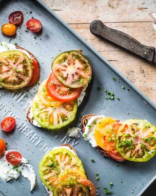 Vier Scheiben Brot mit bunten Tomaten belegt auf Holzuntergrund
