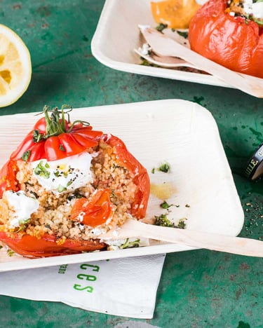Gefüllte Tomaten mit Couscous-Senffüllung und Frischkäse in Holzschälchen mit Holzbesteck neben einem Senfglas auf grünem Untergrund