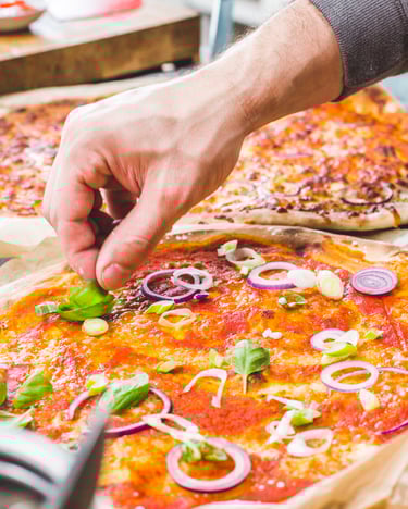 Eine Hand belegt eine Pizza mit Frühlingszwiebeln
