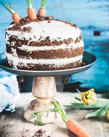 Geschichteter veganer Karottenkuchen auf einer Tortenplatte vor hellblauem Hintergrund