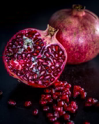 Ein ganzer und ein halbierter Granatapfel mit Granatapfelkernen