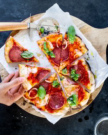 Eine Hand greift nach einem Stück Pizza, die Pizza liegt auf einem Holzbrett