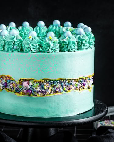 Türkiser Fault Line Cake mit Goldrand und Zuckerstreuseln vor einem schwarzen Hintergrund