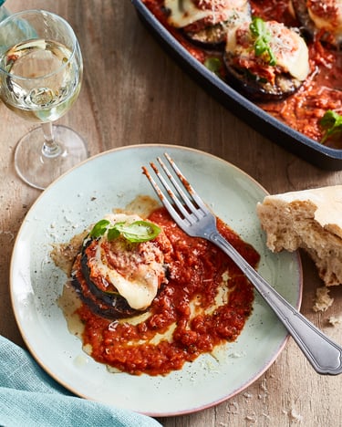 Auberginen-Parmigiana-Türmchen mit Tomatensauce auf Teller, daneben liegt Brot