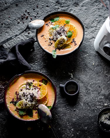 Mandarinen-Möhren-Bowl mit Bananen und Kakaonibs getoppt in zwei Schalen, daneben der KRUPS Blendforce 2in1 mit frischem Möhrensaft.