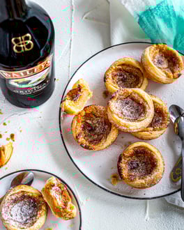 Mehrere Pasteis de Nata mit Baileys auf weißem Teller mit türkiser Stoffserviette.