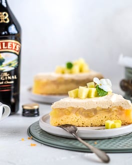 Ein Stück Apfelkuchen mit schichtweise Bisquitboden, Apfelkompott und Baileys-Creme.