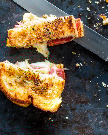 Ein angeschnittenes Grilled Cheese Pizza Toast auf dunklem Hintergrund neben einem Brotmesser.