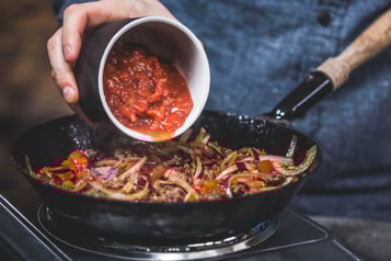 Tomatenpüree wird zu einer Zwiebel-Paprika-masse in eine Pfanne gegeben.