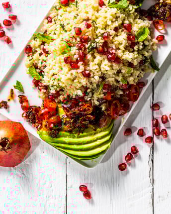 Bulgursalat mit Minze, Avocado und Granatapfelkernen auf einem weißen länglichen Teller und weißem Holzuntergrund