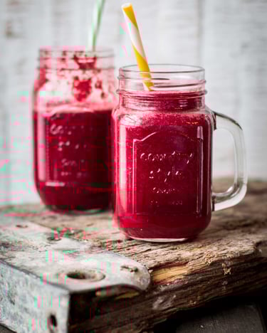 Zwei Glas-Jars mit rotem Smoothie und Papierstrohhalmen auf Holzplanke