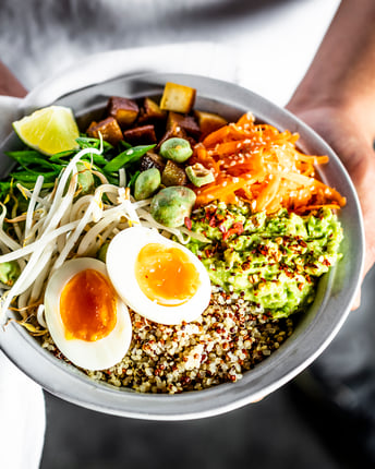 Hände halten tiefen weißen Teller mit Quinoa, Möhren, Tofu und gekochtem Ei