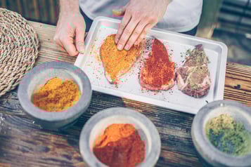 Drei Schweinenackensteaks werden per Hand mit unterschiedlichen Dry-Rub-Mischungen eingerieben