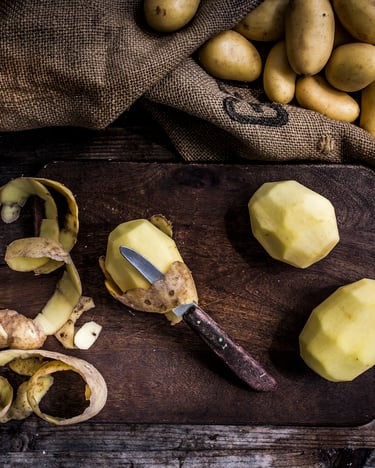 Auf einem Holzbrett liegen geschälte Kartoffeln und ein Messer