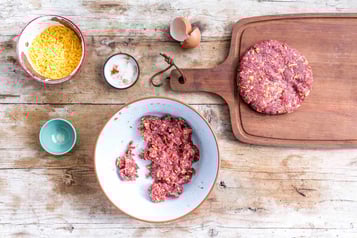 Hackfleisch liegt in einer Schüssel, eine bereits geformte Frikadelle daneben