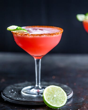 Zwei Margaritagläser mit roter Watermelon Margarita auf Eis, die mit Limettenschalen dekoriert sind