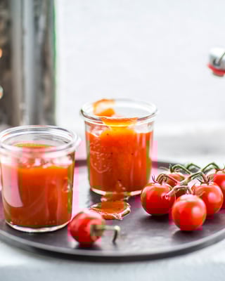 Tomatenketchup in Flasche und Gläser gefüllt mit Tomaten vor Fenster
