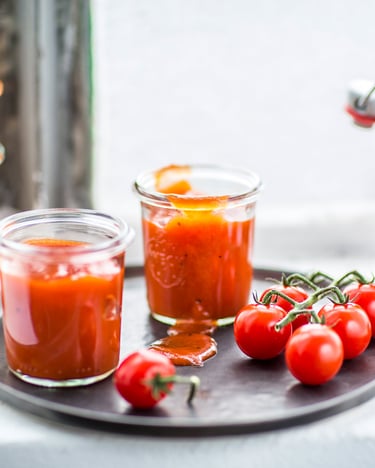 Tomatenketchup in Flasche und Gläser gefüllt mit Tomaten vor Fenster