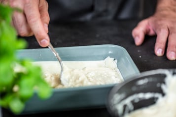 Eine Schicht Béchamel-Masse wird auf Filoteig in einer Auflaufform gegeben