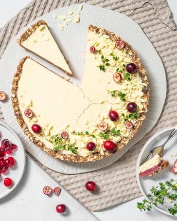 Angeschnittene White Chocolate Cranberry Tarte mit frischen Cranberrys vor hellem Hintergrund
