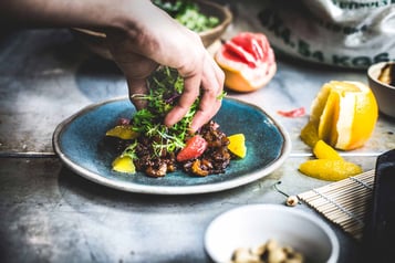 Auf einem blauen Teller wird Salat und Ente angerichtet.