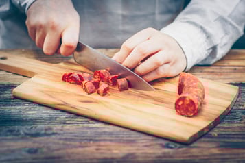 Chorizo wird auf einem Holzbrett gewürfelt