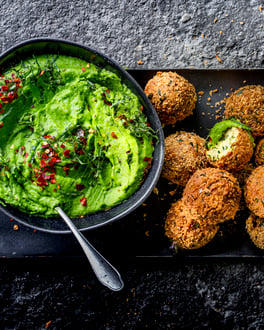 Falafelbällchen auf schwarzem Teller mit einer Schale Erbsen-Hummus.