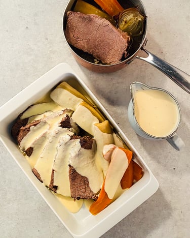 Tafelspitz, Gemüse und Sauce in einer weißen Auflaufform.Daneben stehen eine Sauciere und ein Topf mit Tafelspitz.