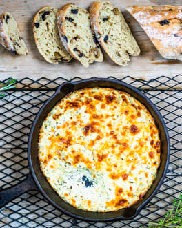Oliven-Ciabatta mit Ricotta-Dip in Pfanne auf Holzuntergrund