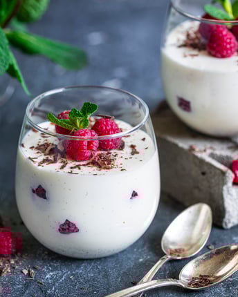 Panna Cotta mit Himbeeren und MInze in Gläsern auf dunklem Grund