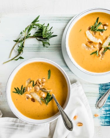 Auf einem weiß-blau lackiertem Holzbrett stehen zwei Schüsseln mit Linsensuppe.