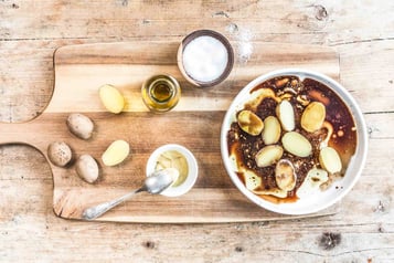Auf einem Holzbrett liegen Kartoffeln, weitere Kartoffeln befinden sich in einer weißen Schüssel daneben.