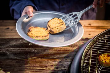 Gegrillte Süßkartoffelscheiben werden mit einem Pfannenwender auf einen tiefen Metallteller gelegt.