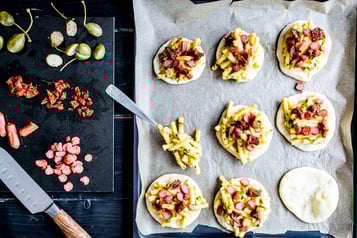 Mehrere Mini-Pizzen liegen ungebacken auf einem Backblech.