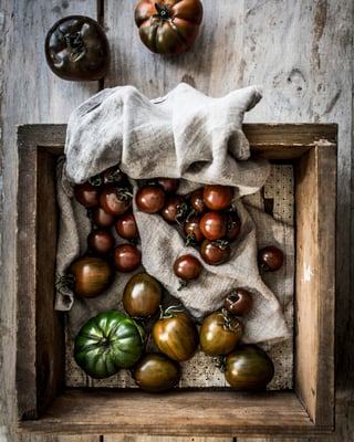 schwarze und grüne Tomaten in einer Holzkiste mit einem Leinentuch darin