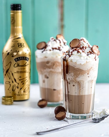 Zwei große Gläser mit Frappé, Sahnehäubchen, Schokokugeln und Baileys Chocolat Luxe.